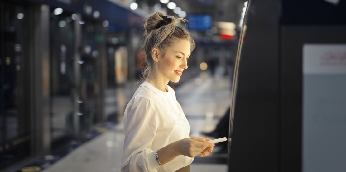 Woman using an outdoor ATM at night, holding a bank card and smiling while interacting with the machine.