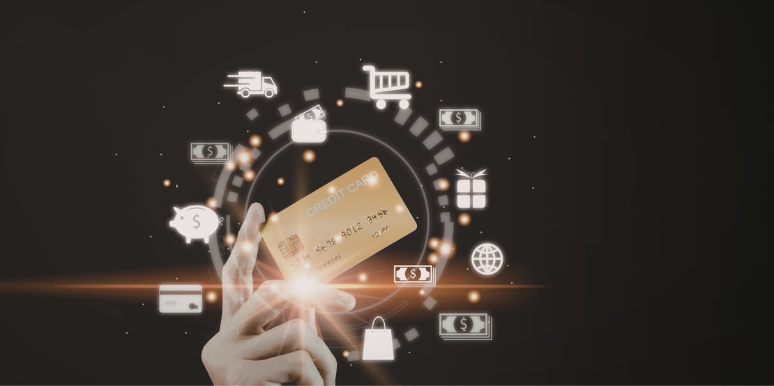 Hand holding a glowing credit card surrounded by digital payment and shopping icons (wallet, cart, cash, gift, globe) on a dark background, symbolizing online transactions and e-commerce.